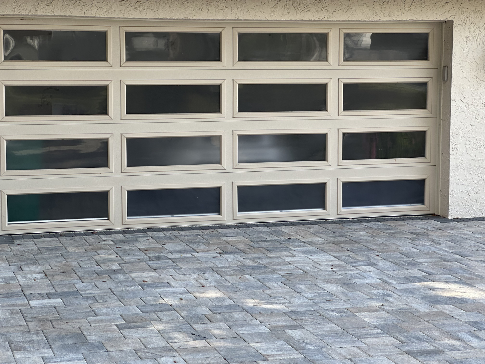 Modern aluminum and frosted glass garage door above a paver driveway
